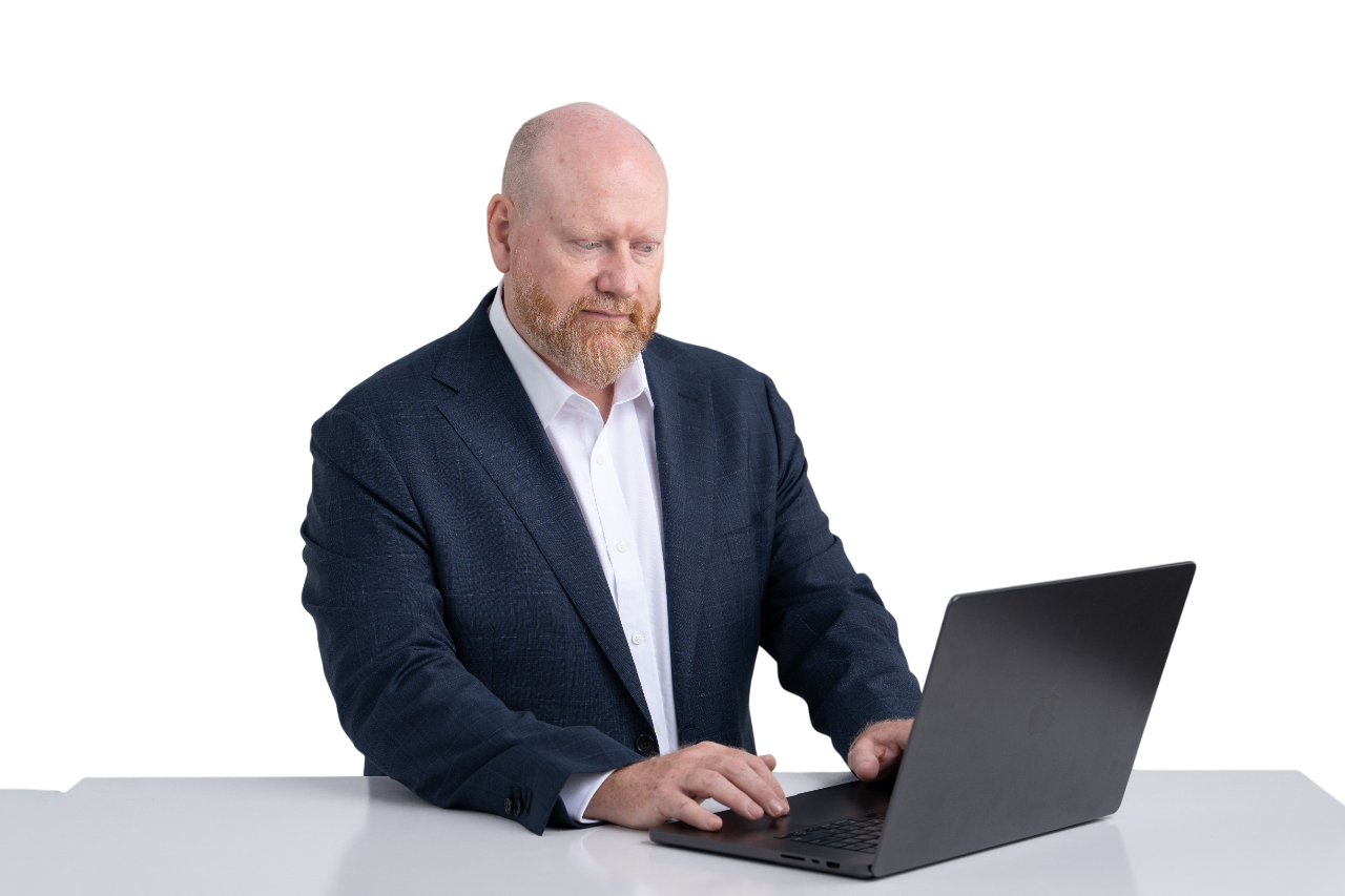 Christian Byron, Co-Founder of Sphere Innovations, wearing a navy blazer and white shirt working on a laptop